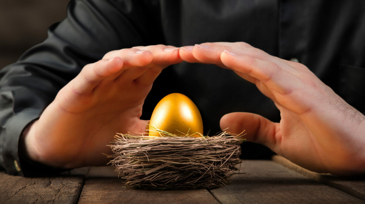 Protecting Hands Over Golden Nest Egg On Wooden Table - Investment Protection Concept