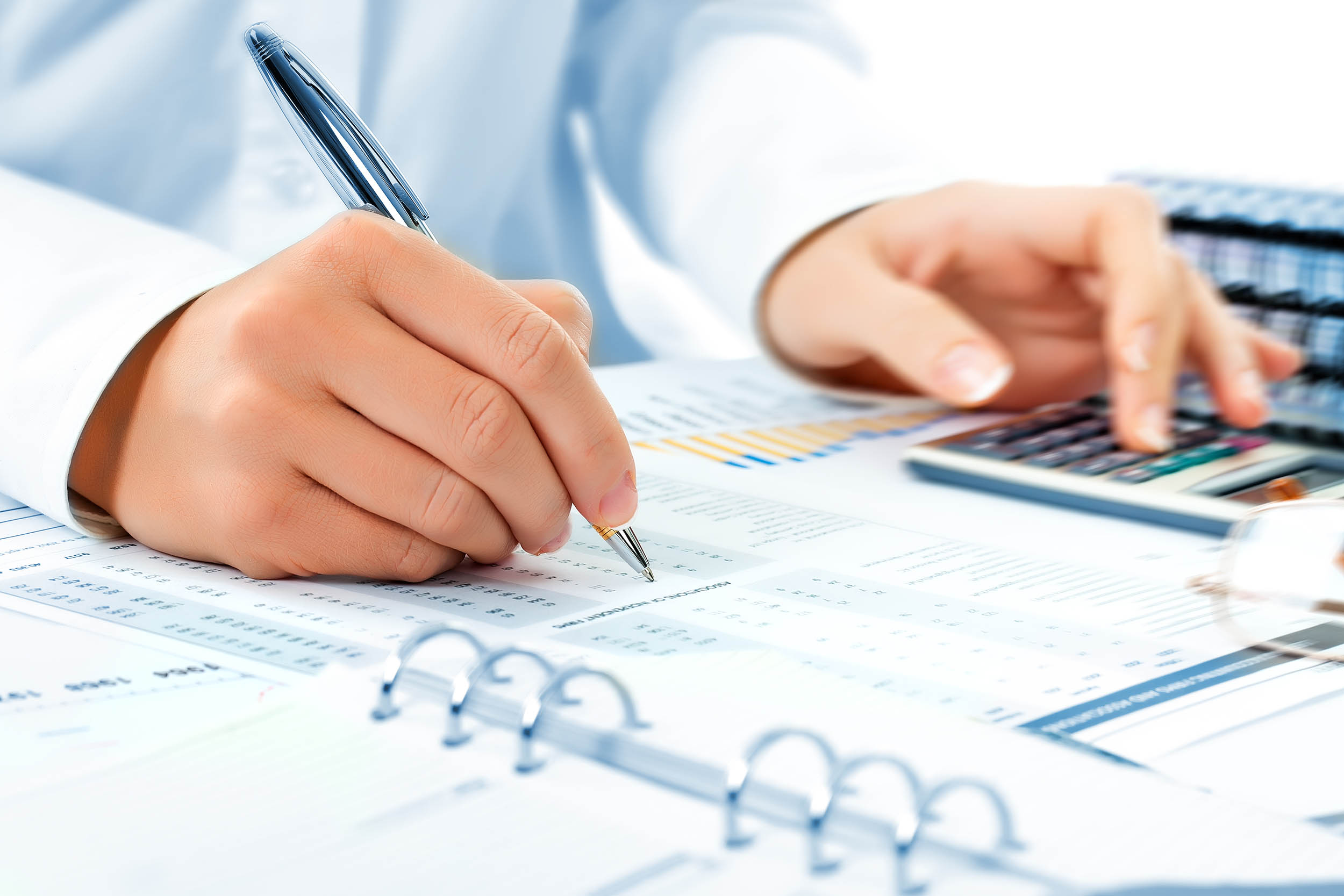 Bookkeeper using a calculator using a pen to record numbers for a small business