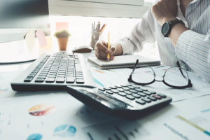 CPA Bookkeeper writing with a pencil using a calculator and keyboard