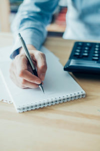 Bookkeeper writing on a pad calculator on the table