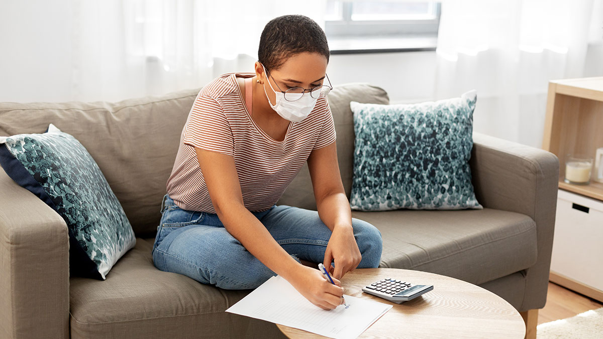 woman doing taxes during the pandemic wearing a mask at a table with a calculator