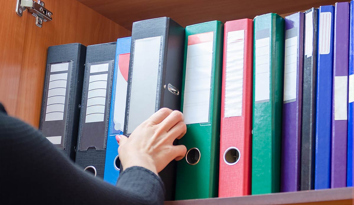 business file binders organized on a shelf woman's hand reaching for one