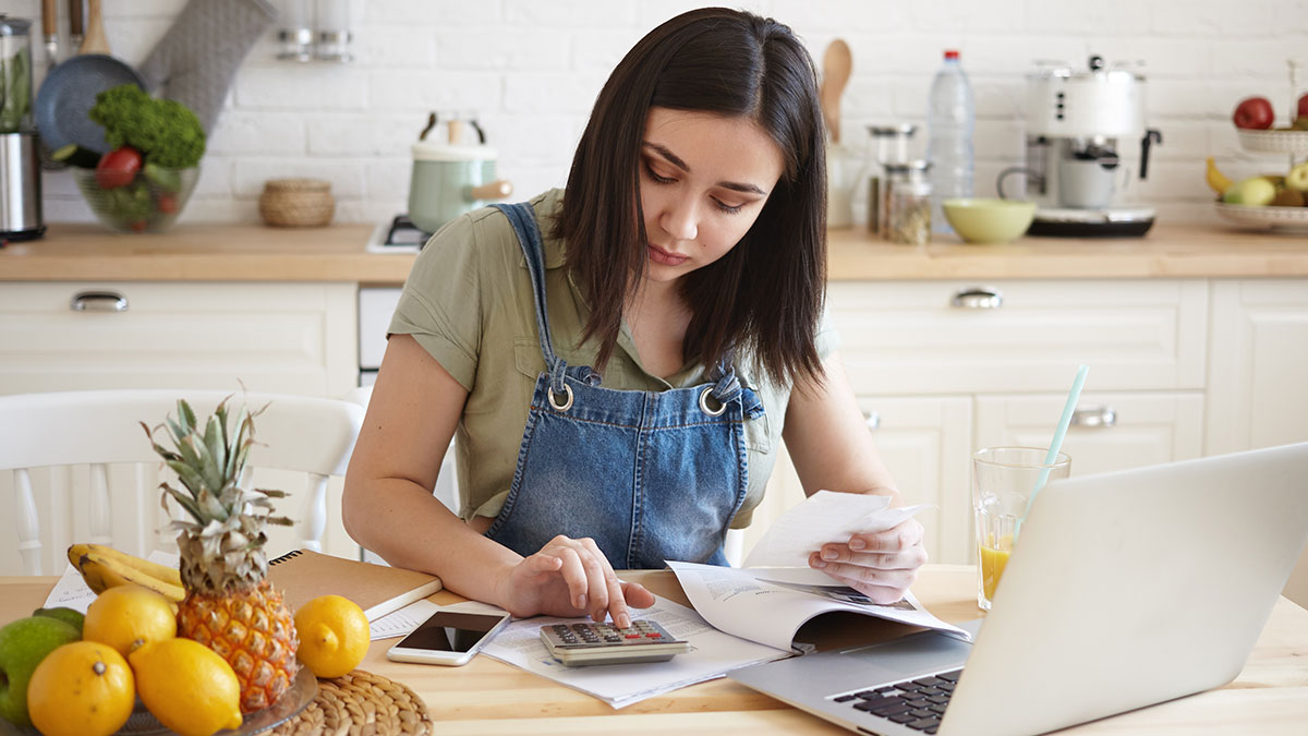Young woman sitting at her kitchen table paying bills