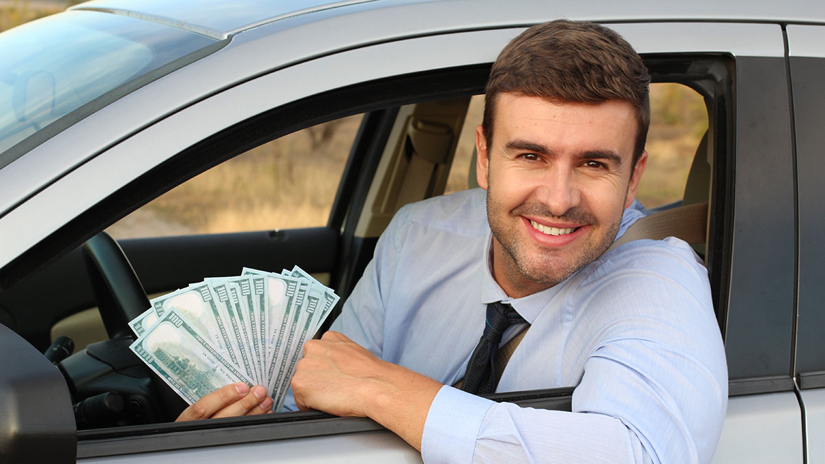 young man wearing a button up shirt and tie holding dollar bills leaning out the car window enjoying his vehicle expense deduction