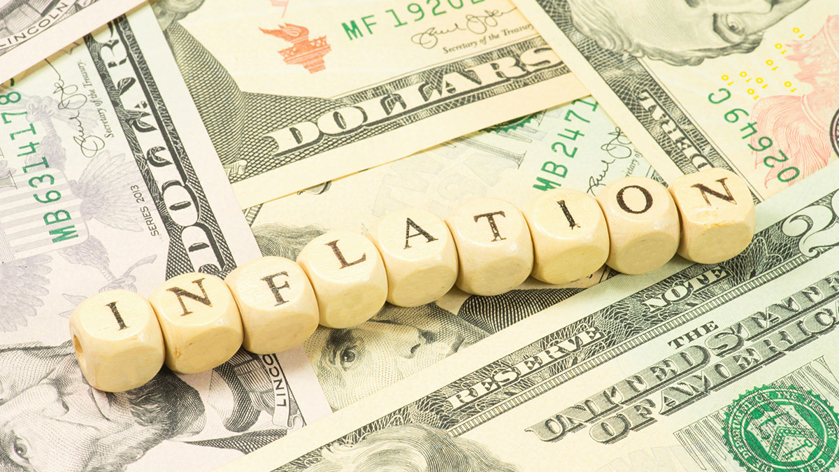 inflation spelled with wooden blocks sitting atop a pile of money