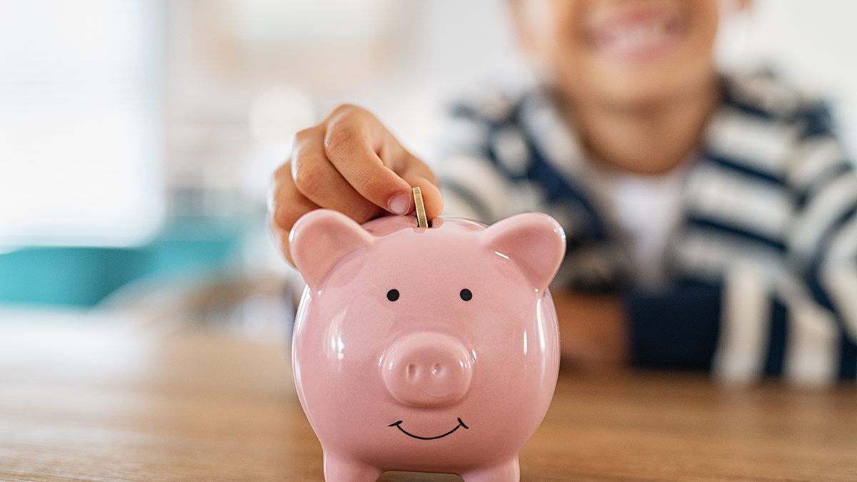 smiling child sitting at a table putting coins in a piggy bank