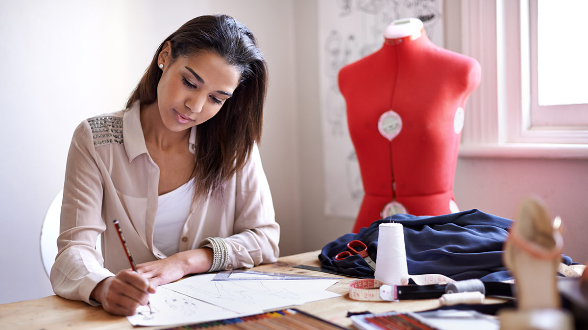 sole proprietor fashion designer sitting at a table drawing sketches clothing mannequin in the background