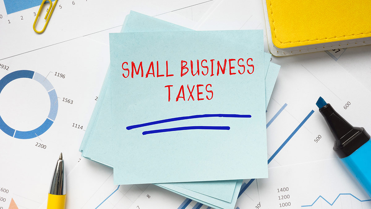 sticky note on a desk that says Small Business Taxes with pens and charts