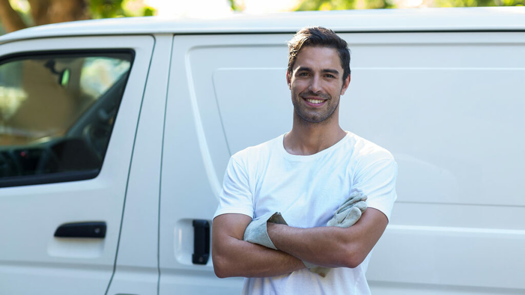 confident young painter standing with his arms crossed in front of his white commercial vehicle van