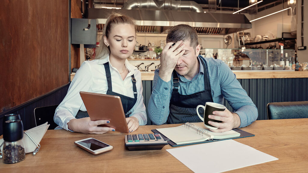 male and female business owners stressed about not paying taxes on time sitting at a wooden table with paper and calculator