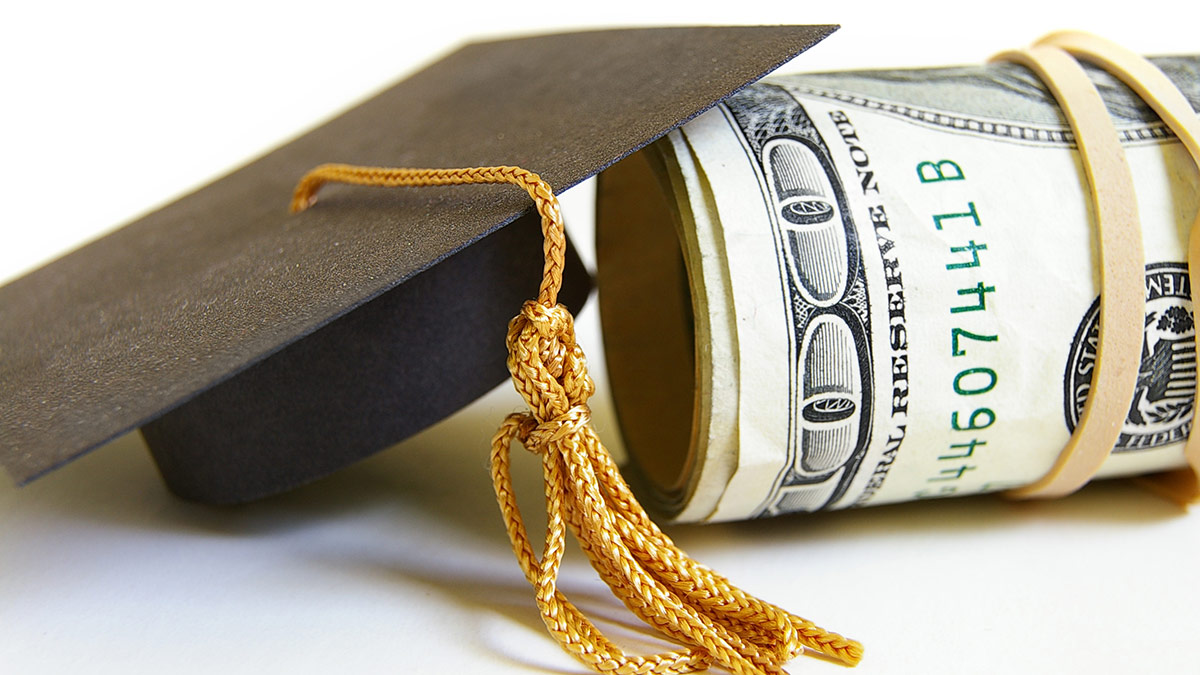 graduation cap and roll of bills on a tabletop scholarship money