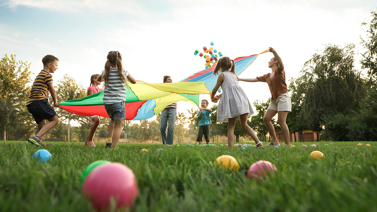 children playing at summer camp on a grassy field with a colorful parachute and balls