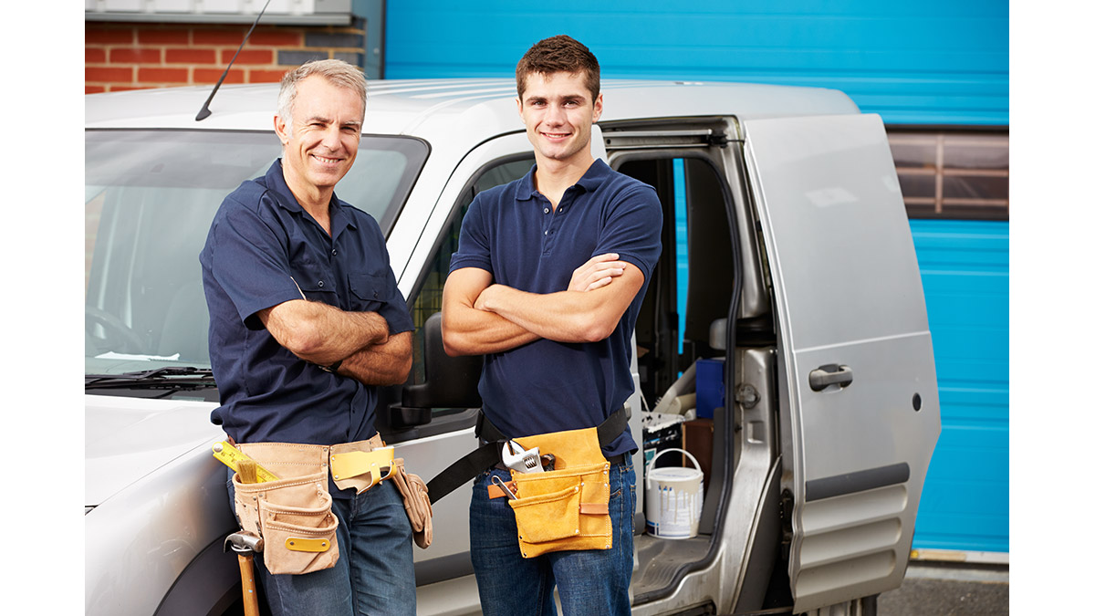 father and son business owners standing with arms crossed in front of a white van with tool belts