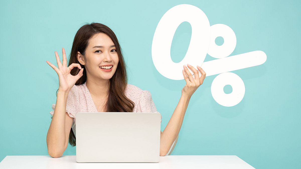 young woman sitting at a desk holding a 0% financing sign on bright teal background