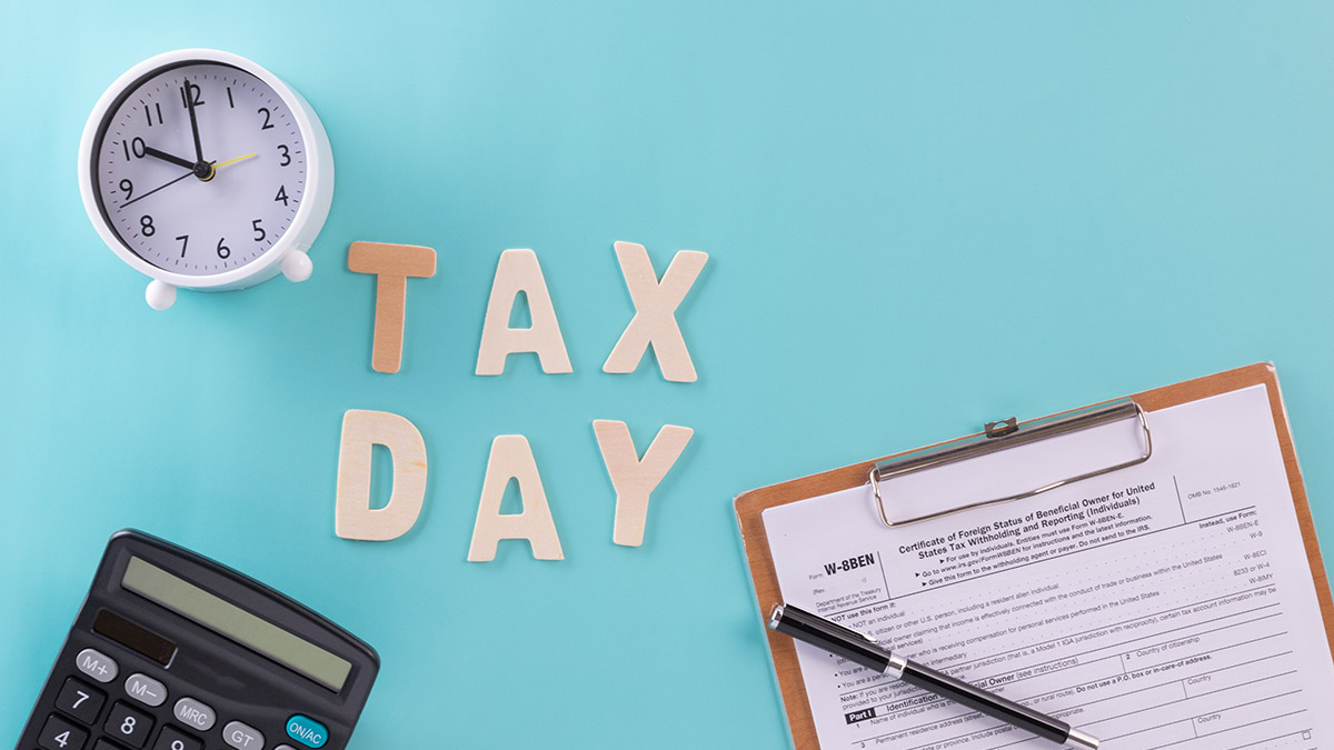 The words tax day on a desk with a calculator, alarm clock, and tax forms